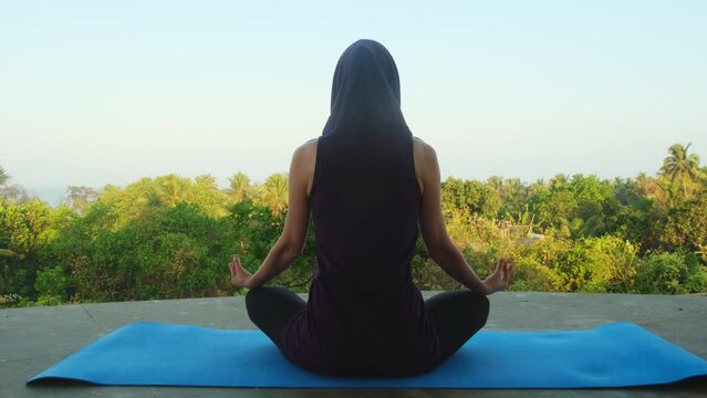 Adult concentrated woman doing yoga practice with deep breath sitting in lotus position outdoors. Female morning meditation in a temple for wellbeing and mental health.