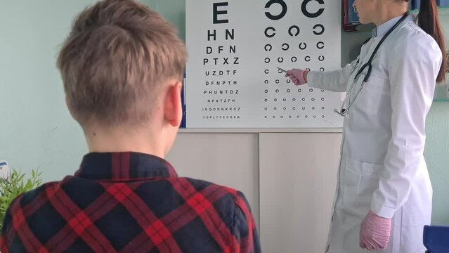 Ophthalmologist holds pen to check vision of teenage boy child. Eye test chart and vision test for adults and children