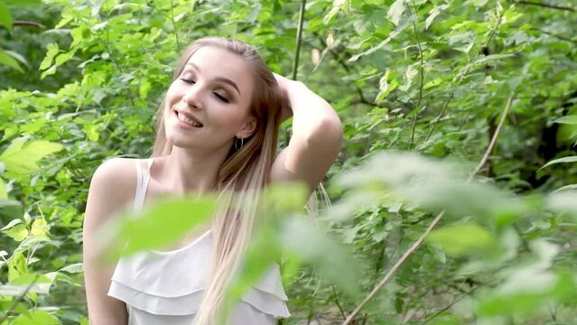 A beautiful lady walking through a summer park enjoys the green sunny nature close-up. Gorgeous girl walking through the greenery of the garden. The concept of a happy and carefree life.