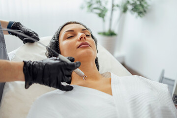 Beautiful caucasian young woman is doing a mole removal procedure in a modern beauty cosmetic...