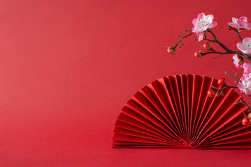 New Year symbolism: A side view composition featuring pink sakura blossoms, and fan. Against a red...