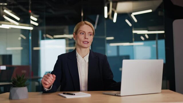 Calm businesswoman completes work, sitting at workplace with hands folded in a mudra gesture. Stress reduction activities, meditating or practicing yoga breathing exercises during workday in office.