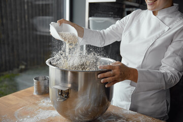 Closeup female baker chef mixing flour for sourdough in metal bowl