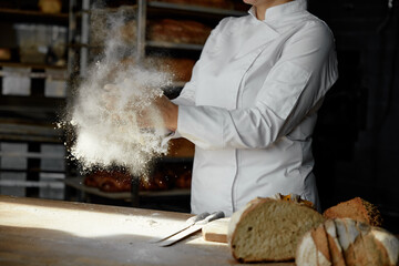 Closeup female chef hands clapping in cloud of powdery flour over table