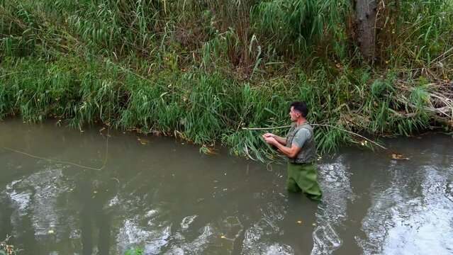 Fisherman in a vest and waders tucked into the river casting and retrieving his rat tail fishing rod.