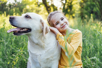 Cute little girl hugging her pet dog - golden labrador retriever.
