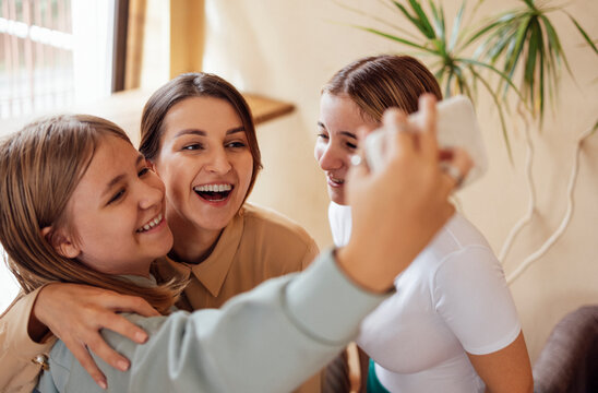 Three cute smiling teen girls hugging and taking a selfie.