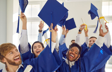 Group of smiling happy overjoyed graduates students standing indoors with hands up holding diplomas...