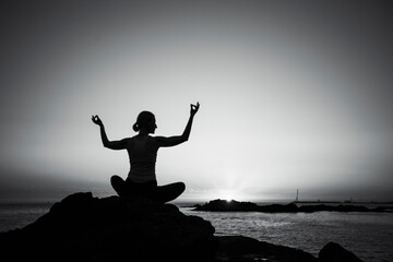 Silhouette of a yoga woman on the shore. Black and white photo.