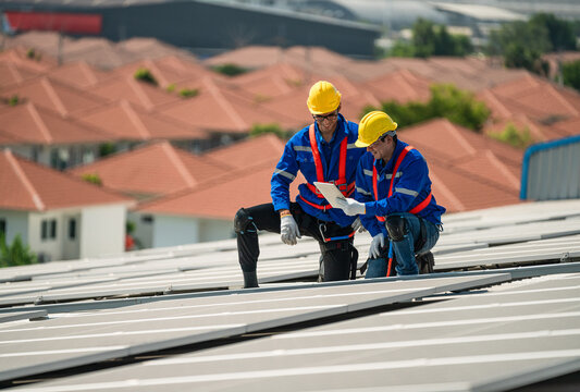 Men technicians carrying photovoltaic solar modules on the factory roof. Engineers in helmets installing solar panel systems outdoors. Concept of alternative and renewable energy.