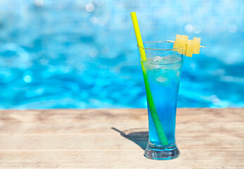 Glass with a bright blue lagoon cocktail on the table by the pool
