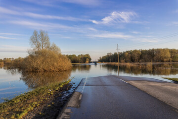 We drive a car along a flooded road, the river overflows along the road, spring flood