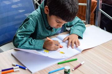 Smart Indian little boy perform thumb painting with different colourful water colour kit during the summer vacations, Cute Indian Kid doing colourful thumb painting drawing on wooden table