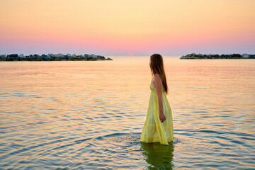 A young woman in a bright yellow dress meets the sunrise, joyfully runs through the sea water.