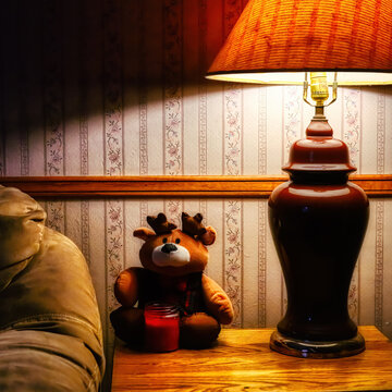 A small stuffed animal sits on the end table under the warm glow of a lamp in our living room.  Reindeer decoration and a small candle next to the couch help make the holiday season festive. 