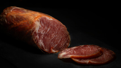 Lomo ibérico. Iberian loin from Spain on a black background prepared to eat. Iberian bait loin sausage stuffed and cured in the cellar. Delicious cured Iberian pork loin. Copy space - obrazy, fototapety, plakaty