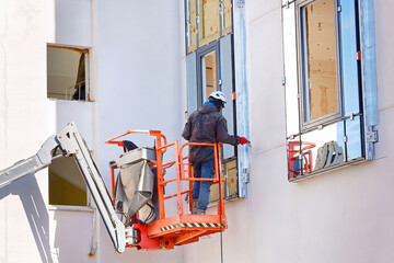 Man in lift bucket caulk, seal exterior window with putty knife, maintain exterior window. Worker...