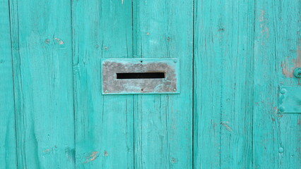 Gap in the fence designed to receive letters. The wooden fence is painted in a vibrant turquoise color