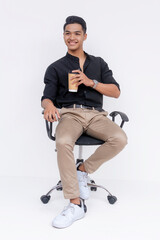 A confident and handsome Filipino man sitting relaxed on an armchair. Holding a cup of coffee. Studio shot isolated on a white background.