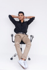 Handsome and youthful asian man sitting on an office chair. Hands up on neck for support while slouching a bit. Studio shot isolated on a white background.
