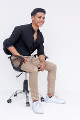 A confident and handsome Filipino man sitting while leaning forward on an office chair. Studio shot...