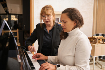 Young adult Asian female pianist, music teacher teaching piano and music lesson to a woman - obrazy, fototapety, plakaty