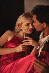 joyful blonde woman in fashionable dress looking lovingly at her african american boyfriend