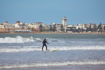A young female surfer gracefully rides the waves on her board along the shores of Essaouira, Morocco