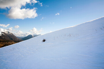 Mountain chains with a snow-covered smooth slope in the foreground.