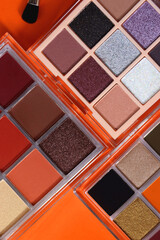 Colorful eyeshadow palettes and make up brush on orange background. Top view.