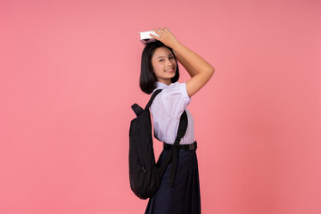Asian female student presenter for world education Lift the textbook on your head. carrying a school bag Study at famous schools and tutoring institutes Taking photos in a pink background studio
