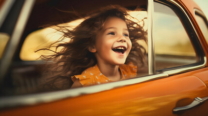 Happy young girl sitting in a driving or moving car, smiling and looking through the open window. Excited cute female child with curly hair enjoying the summer vacation road trip, sun shining