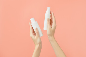 A womans hands holding a white cosmetic bottles on a peach background. Beauty treatment concept