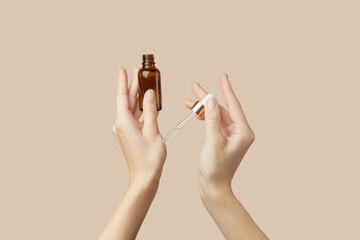 A womans hands holding a brown bottle of serum on a beige background. Body care