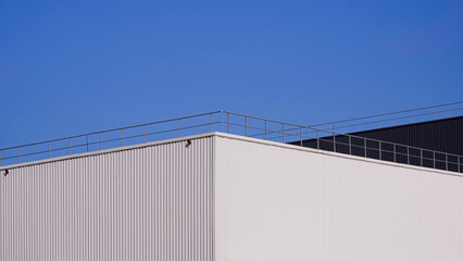 Modern white and black aluminium corrugated factory buildings with steel fence on rooftop against blue clear sky background