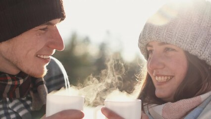 Close-up of a guy and a girl smiling.Young couple happy together on vacation in nature holding hot drink in their hands steaming in frosty winter air. Brain-to-heart conversations and heart-to-heart