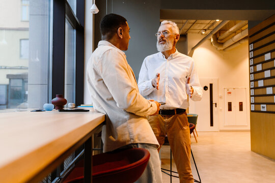 Confident businessman talking to younger male colleague while standing in office space
