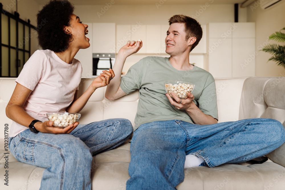 Wall mural Happy couple having fun and throwing popcorn while watching movie at home