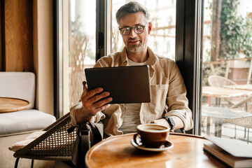 Portrait of smiling man making video call via tablet while sitting at table in cafe