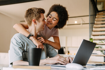 Woman hugging her boyfriend while he working on laptop computer at home