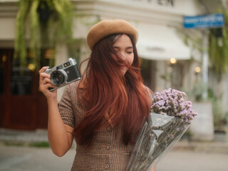 Young woman holds camera and flowers in hand and smiles