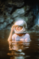 Young woman wearing an astronaut helmet sits with a fern tree.