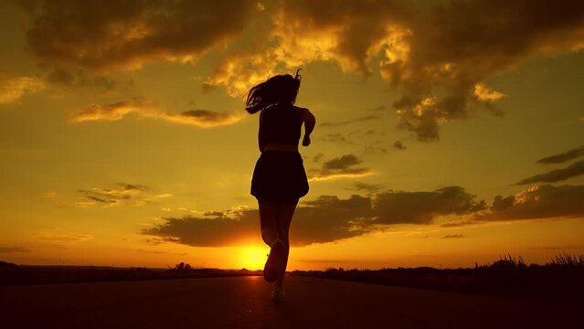 Jogging outside city. Running after sun. Training jogging. Beautiful girl doing fitness, jogging on road in sun. Jogger girl breathes fresh air in nature. Free young woman runs in summer park, sunset