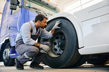 Truck maintenance mechanic inspecting tires of vehicle in workshop.