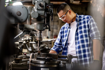 Asian worker in production plant drilling at machine. Professional worker near drilling machine on factory. finishing metal working internal steel surface on lathe grinder machine with flying sparks.