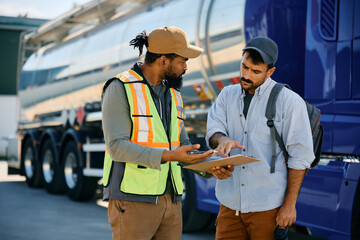 Truck driver and African American dispatcher analyzing shipment list on parking lot. - obrazy, fototapety, plakaty