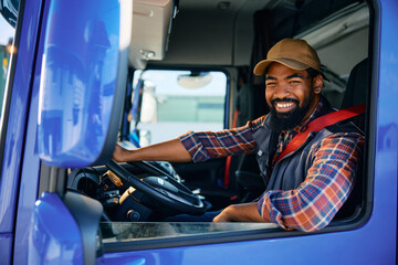 Happy black truck driver behind steering wheel in cabin looking at camera.