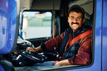 Happy professional truck driver driving truck and looking at camera.