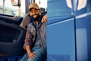 Happy black truck driver sitting in vehicle cabin and looking at camera.