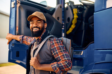 Happy black professional driver getting out of his truck and looking at camera.